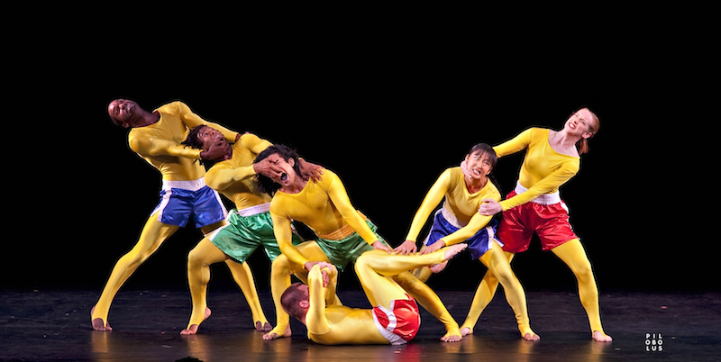 Members of Pilobolus in gold body suits and gym shorts pulling at one another's faces to create a humorous tableau.